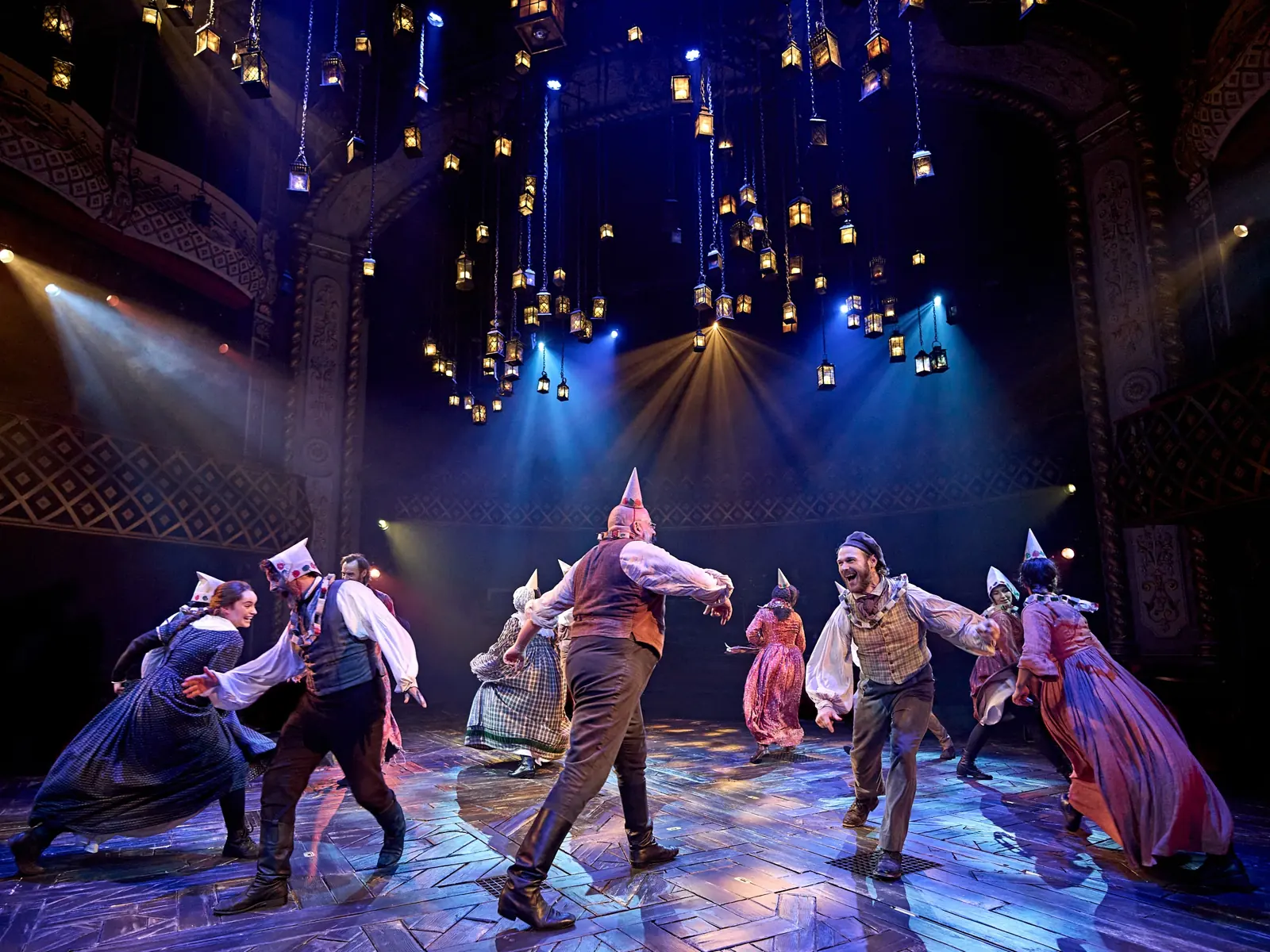 The company dancing in Victorian party clothes beneath lantern light, A Christmas Carol at The Old Vic