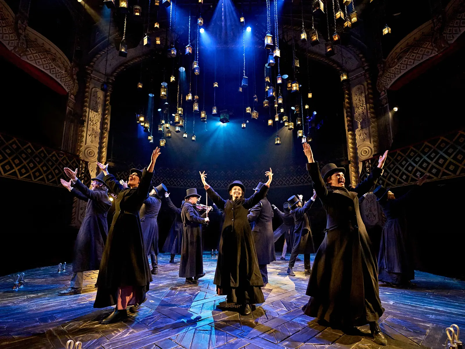 The company in black coats and top hats under hundreds of hanging lanterns, A Christmas Carol at The Old Vic