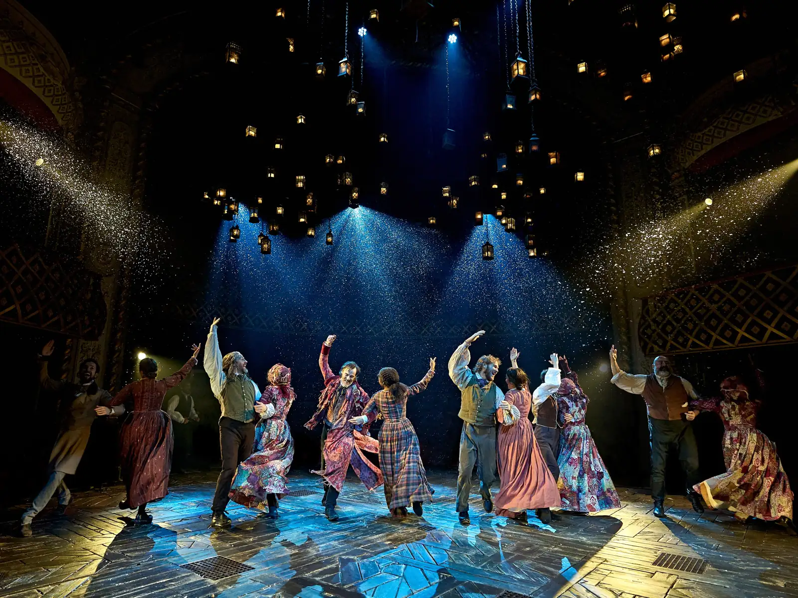 The company dancing as snow falls through the lantern light, A Christmas Carol at The Old Vic