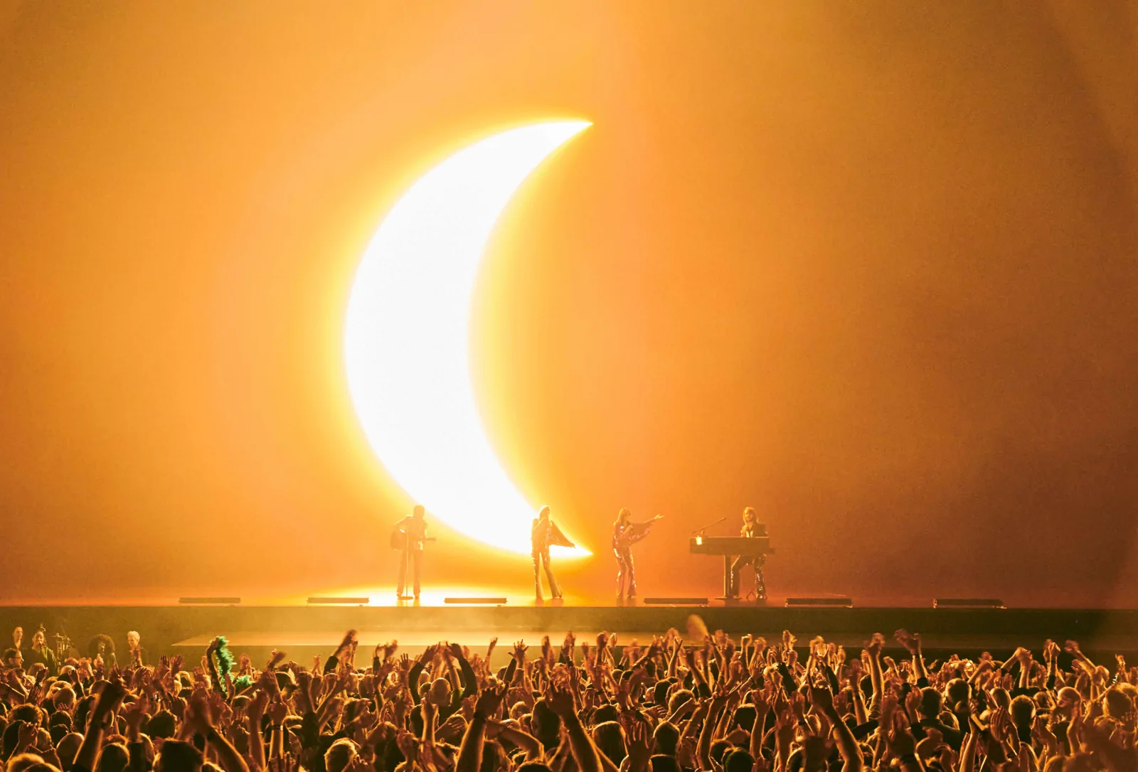 Four figures perform before a huge glowing crescent moon in ABBA Voyage, ABBA Arena