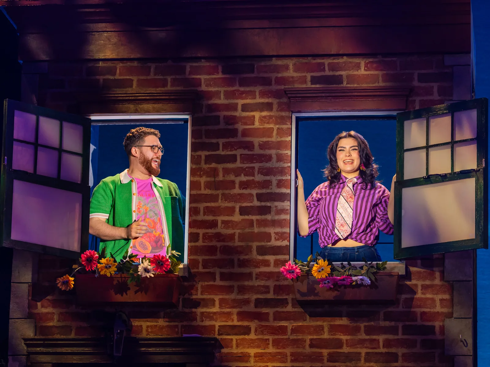 Two neighbours lean from flower-box windows on the brick street in Avenue Q, Shaftesbury Theatre
