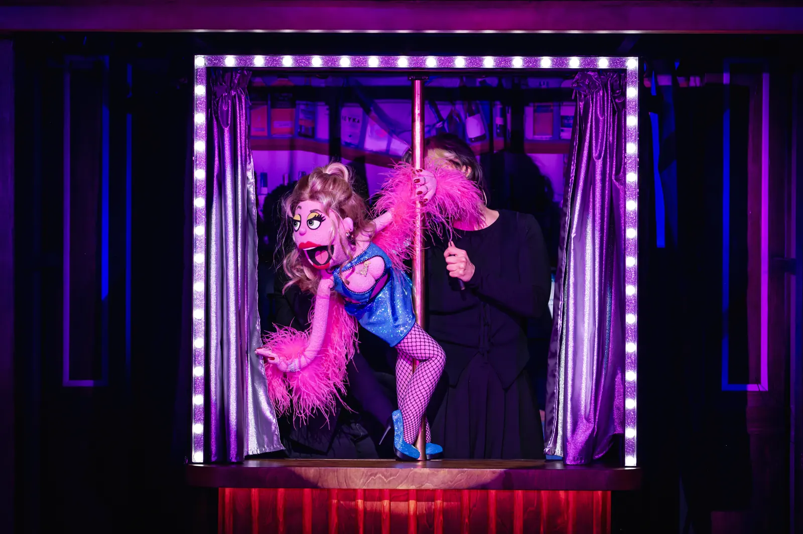 Lucy the Slut swings round a pole in a neon booth, Avenue Q, Shaftesbury Theatre