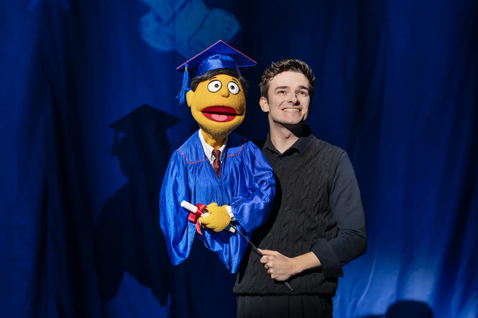 Noah Harrison with a puppet in graduation cap and gown, Avenue Q, Shaftesbury Theatre