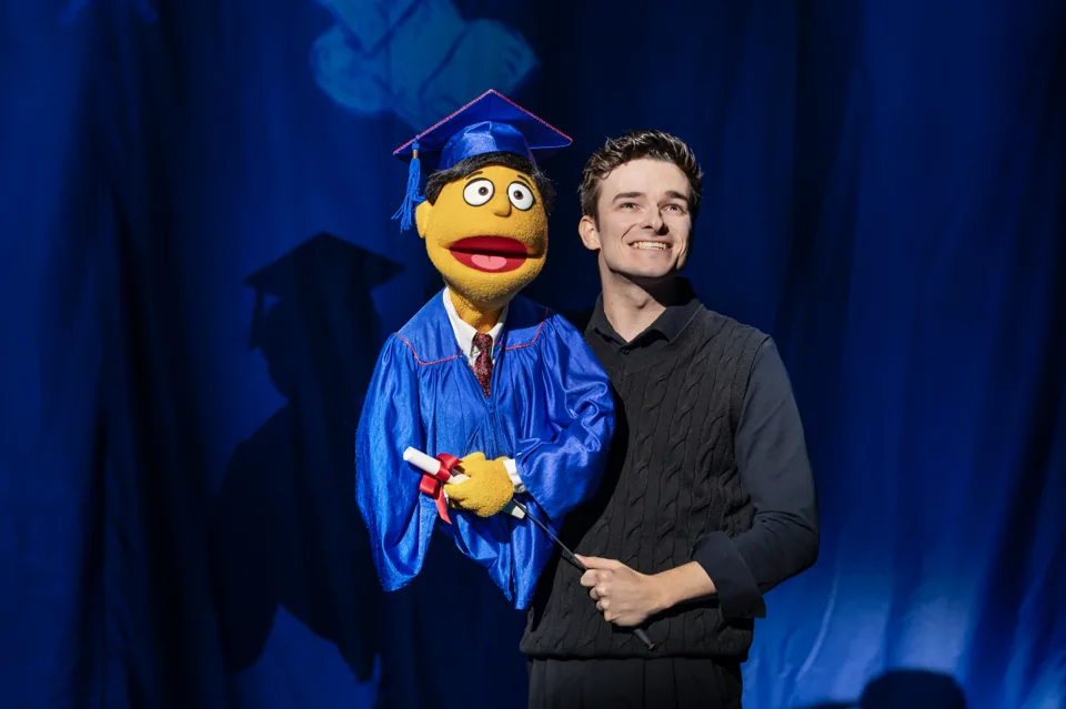 Noah Harrison with a puppet in graduation cap and gown, Avenue Q, Shaftesbury Theatre