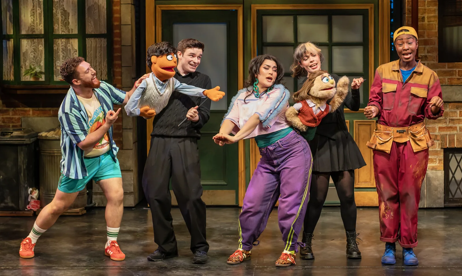 Performers and puppets dance in a line along the street in Avenue Q, Shaftesbury Theatre