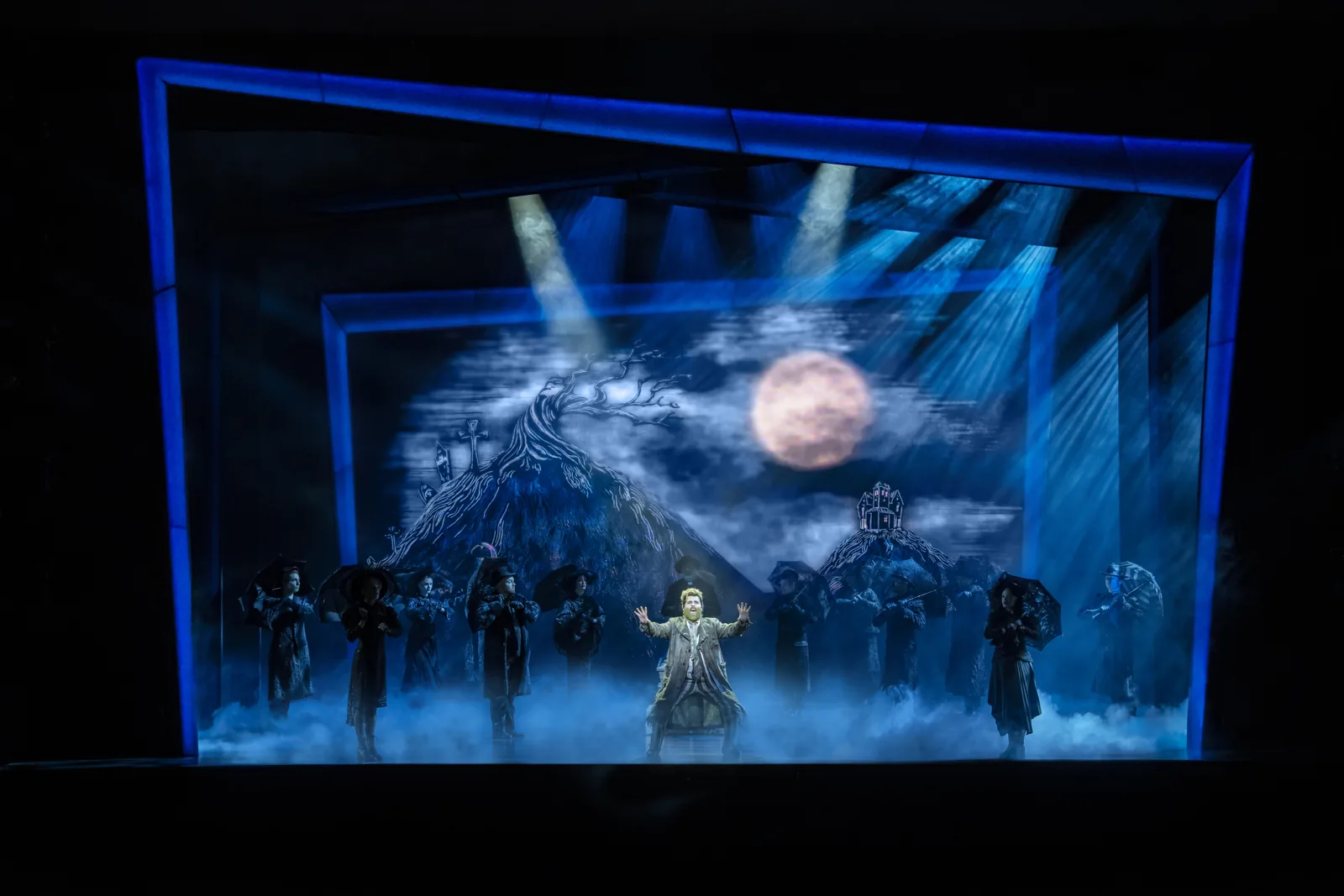 David Fynn as Beetlejuice among umbrella-carrying mourners under a full moon, Beetlejuice, Prince Edward Theatre