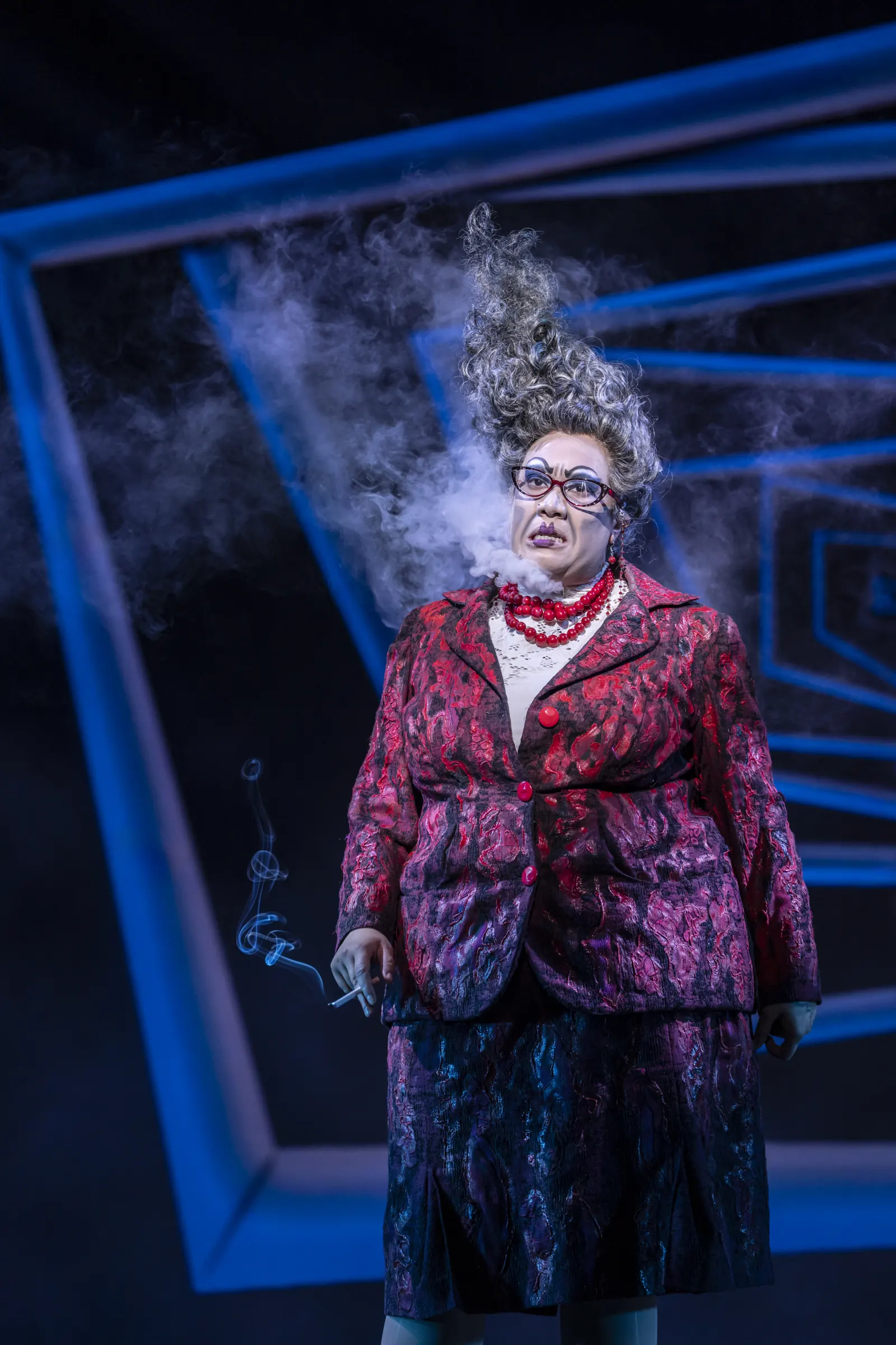 A woman with towering grey hair exhales smoke, Beetlejuice, Prince Edward Theatre