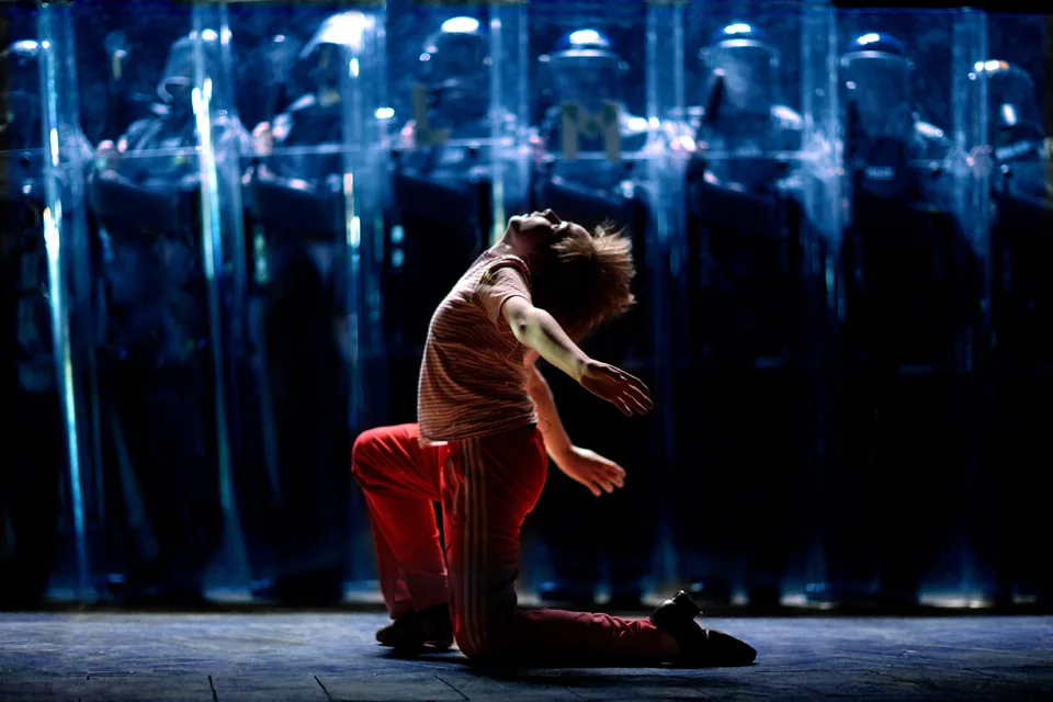 Billy kneels and arches back before police riot shields, Billy Elliot the Musical