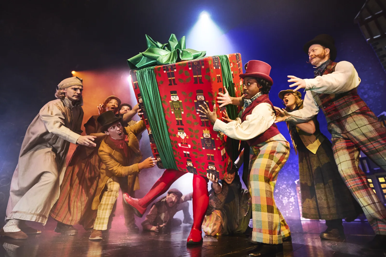 Actors push a giant present with legs, Christmas Carol Goes Wrong, Wyndham's Theatre