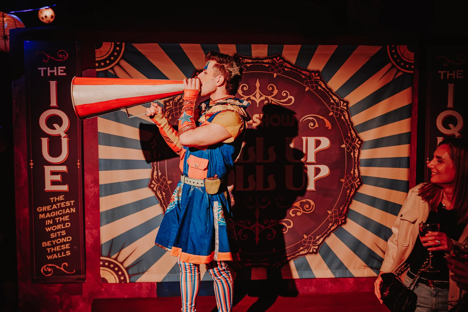 A costumed performer shouts through a red-and-white megaphone beside a guest, Come Alive!, Empress Museum