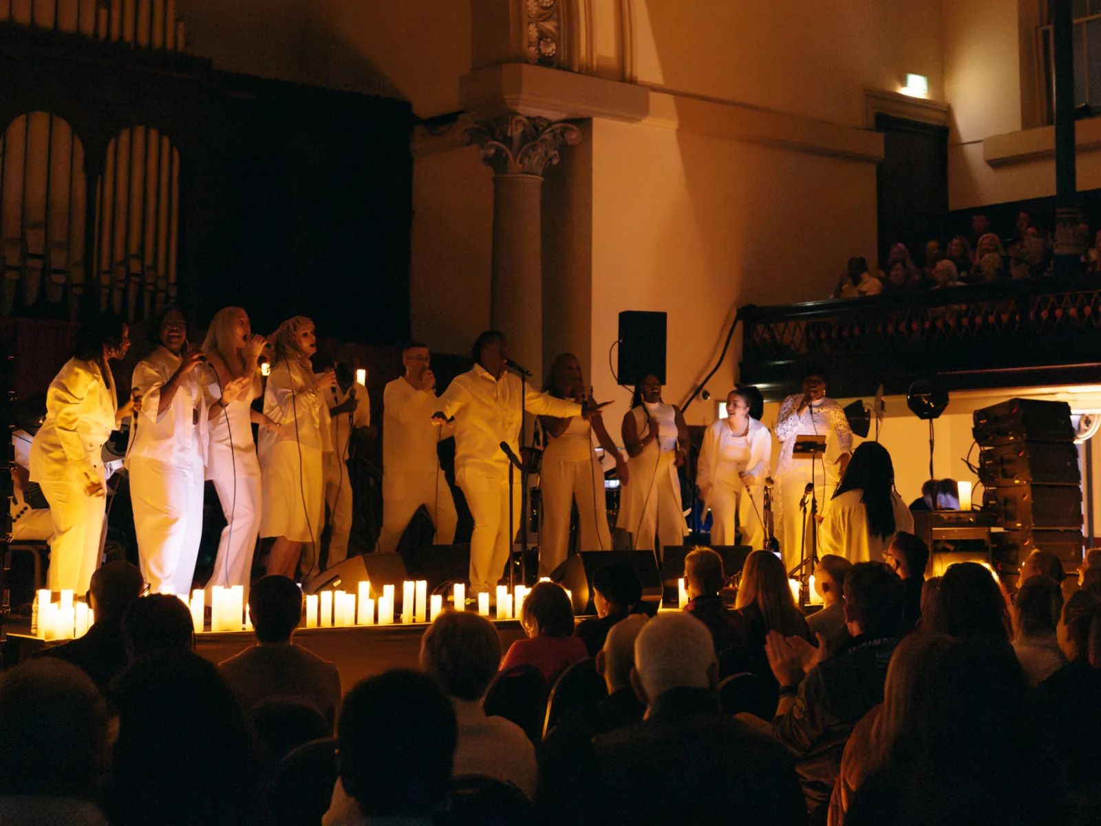 A gospel choir in white sings surrounded by candles, Gospel by Candlelight