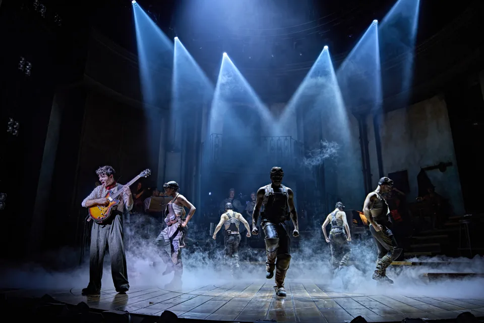 Nathan Sykes as Orpheus and the workers move through haze, Hadestown, Lyric Theatre