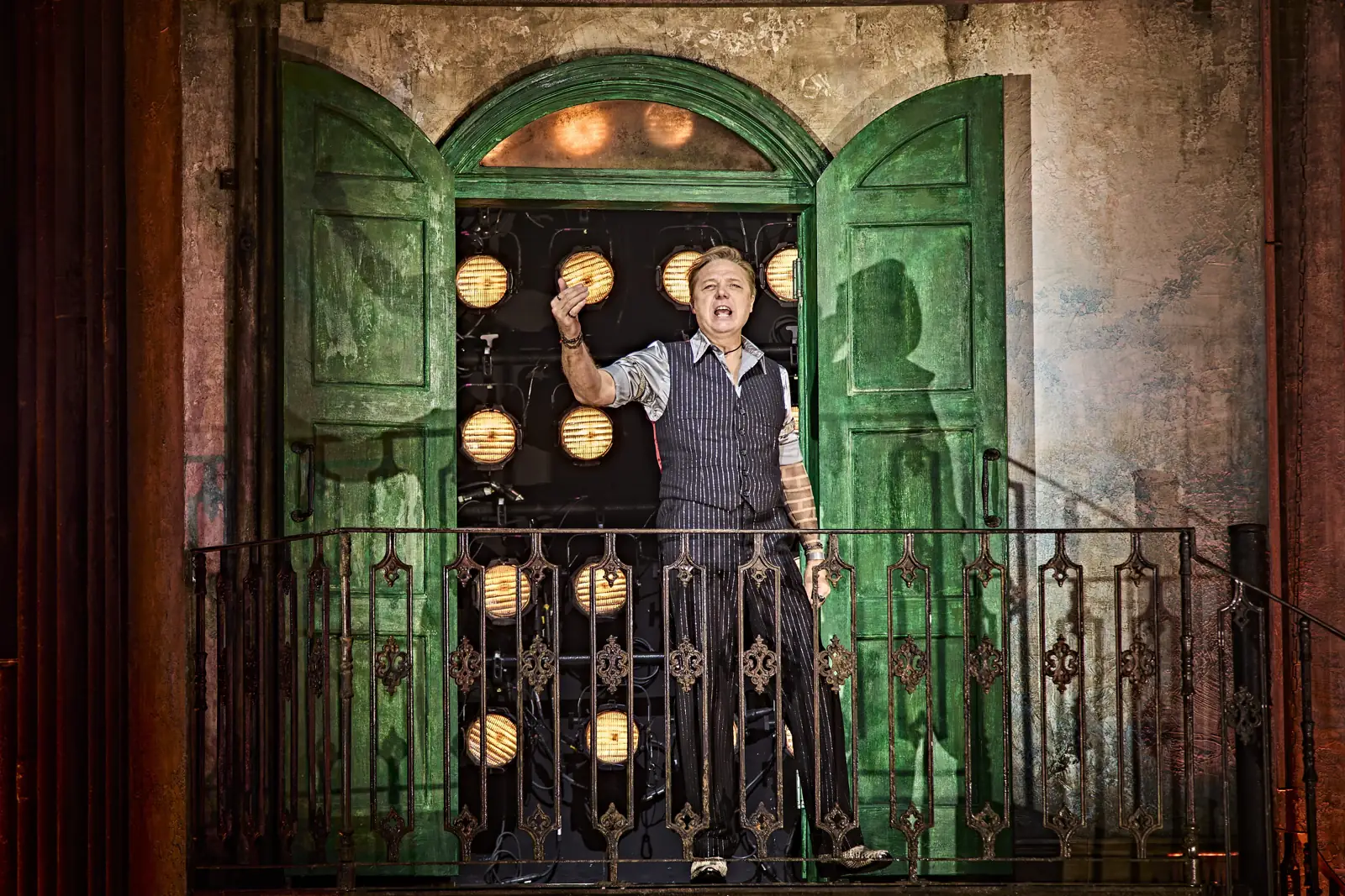 Shaun Dooley as Hades looks down from a balcony between green doors, Hadestown, Lyric Theatre