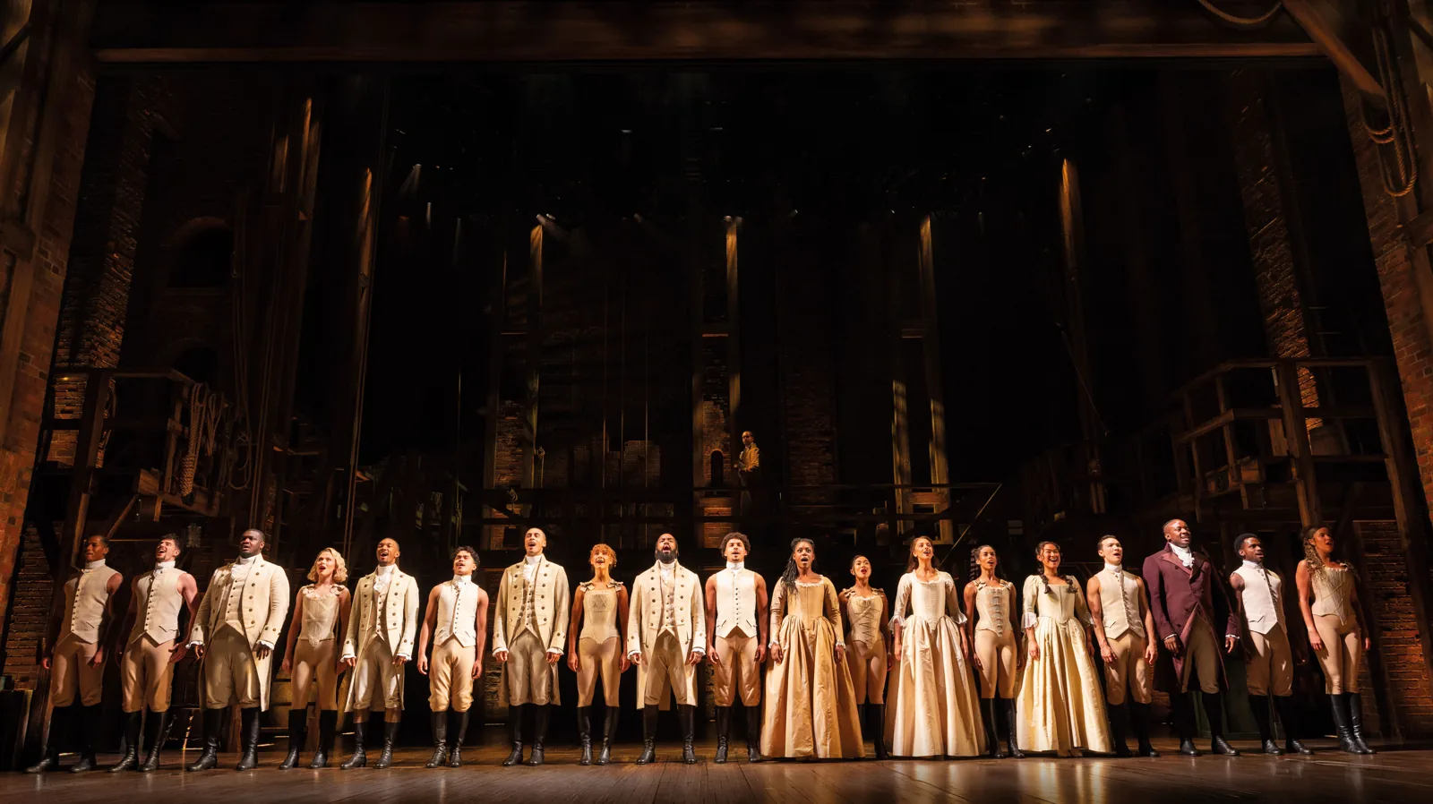 The Hamilton company stands in a line on the stage at the Victoria Palace Theatre