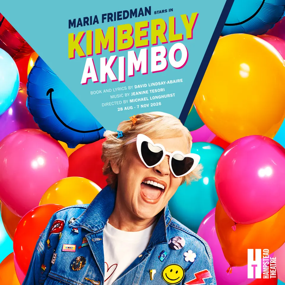 Person in denim jacket with heart-shaped sunglasses surrounded by balloons in Kimberly Akimbo at the Hampstead Theatre