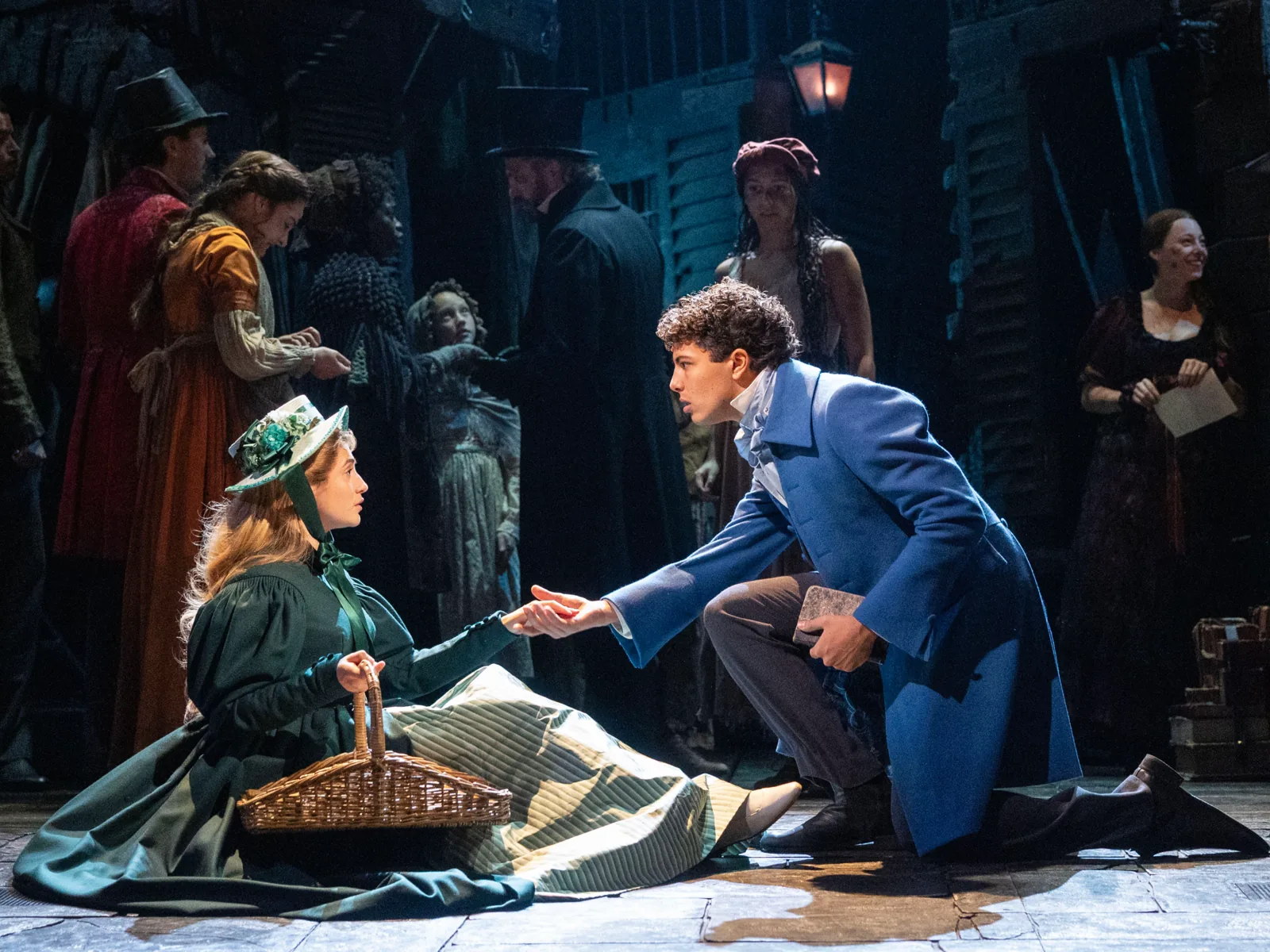 A young man kneels to a woman with a basket in Les Misérables, Sondheim Theatre