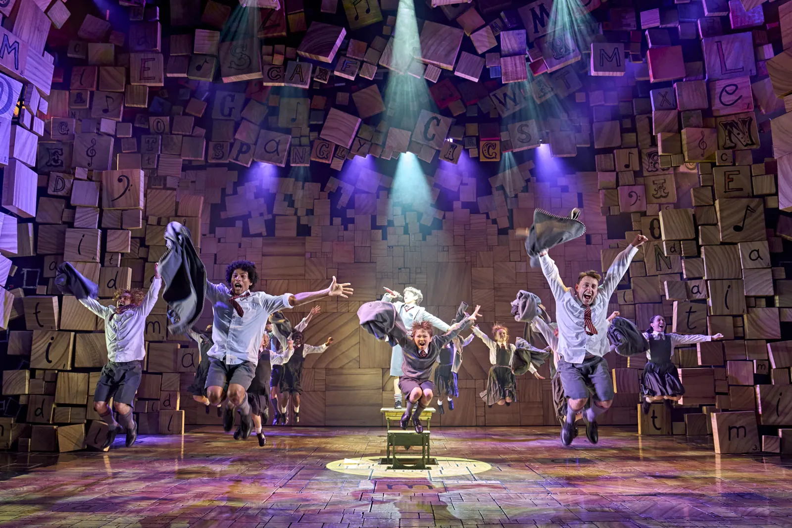 Schoolchildren leap into the air around a desk in Matilda The Musical, Cambridge Theatre