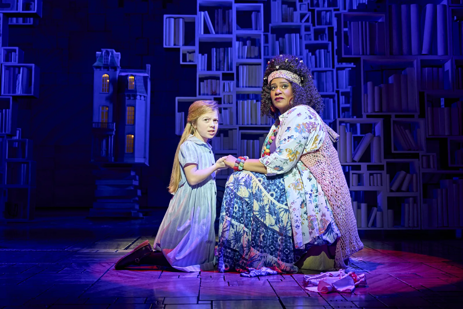 A girl and a woman kneel among bookshelves in Matilda The Musical, Cambridge Theatre