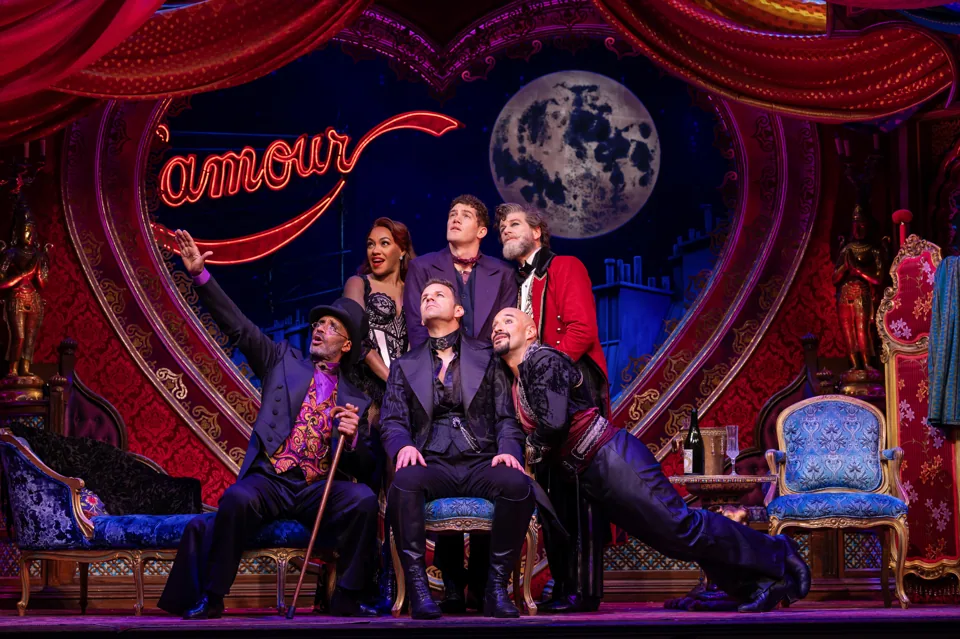 Seven performers gaze up at a painted moon in Moulin Rouge! The Musical, Piccadilly Theatre