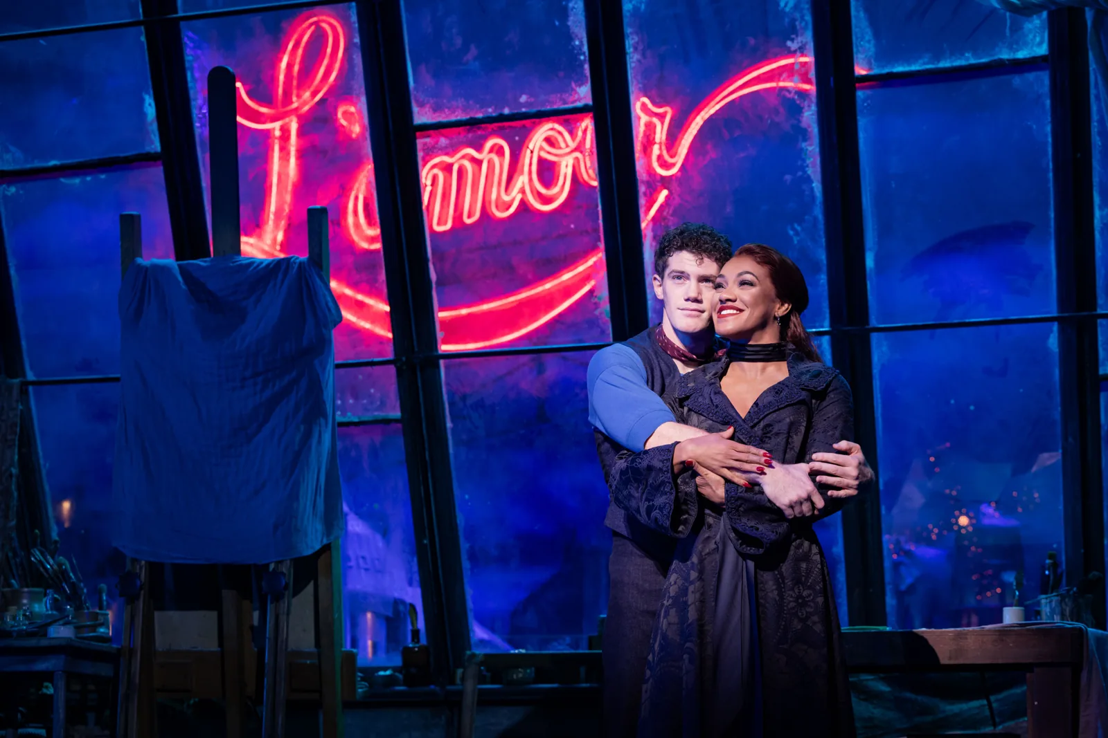 A couple embrace beneath a pink neon sign in Moulin Rouge! The Musical, Piccadilly Theatre