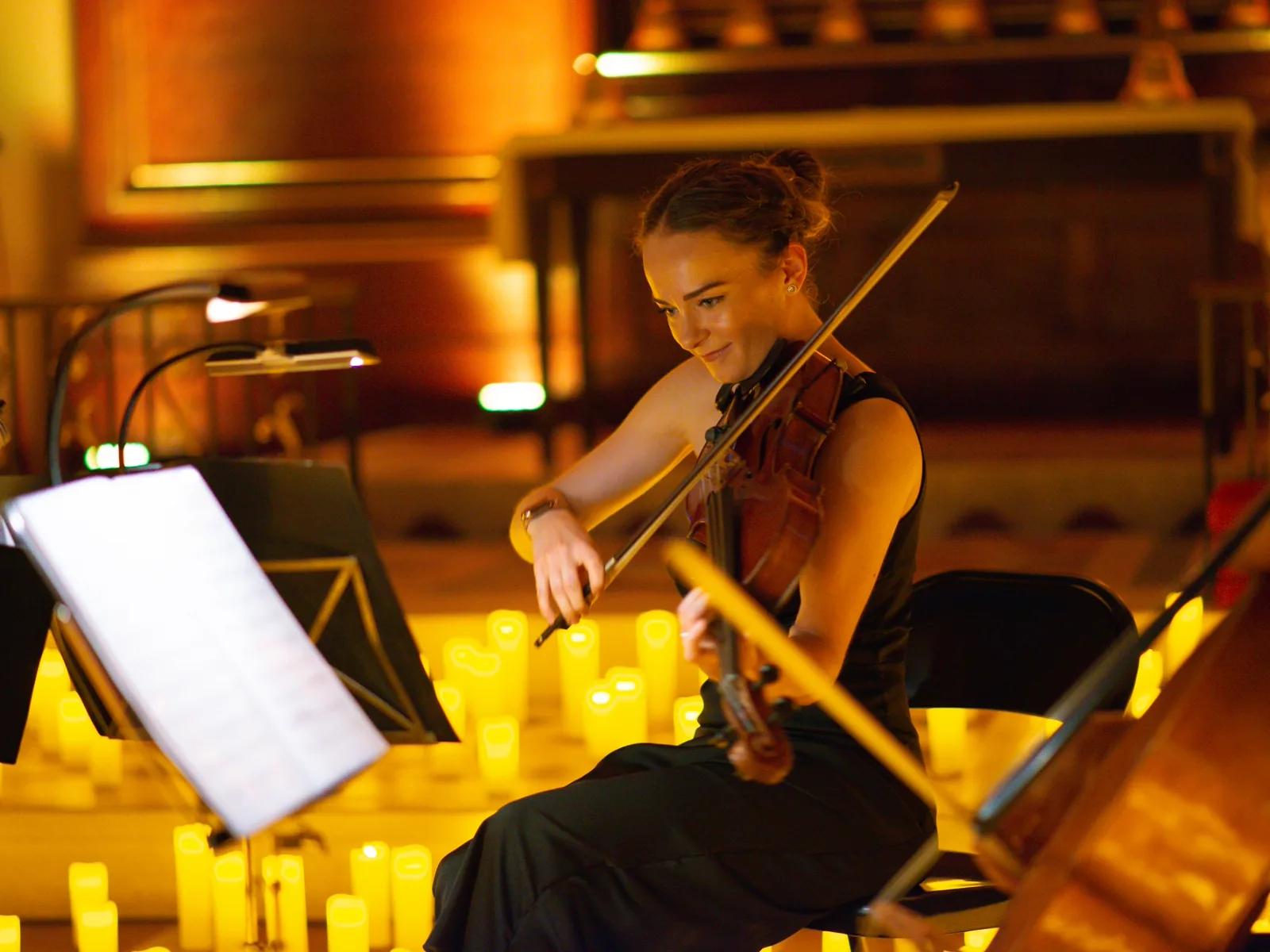 A violinist smiles as she plays among candles at Musicals by Candlelight, The Actors' Church