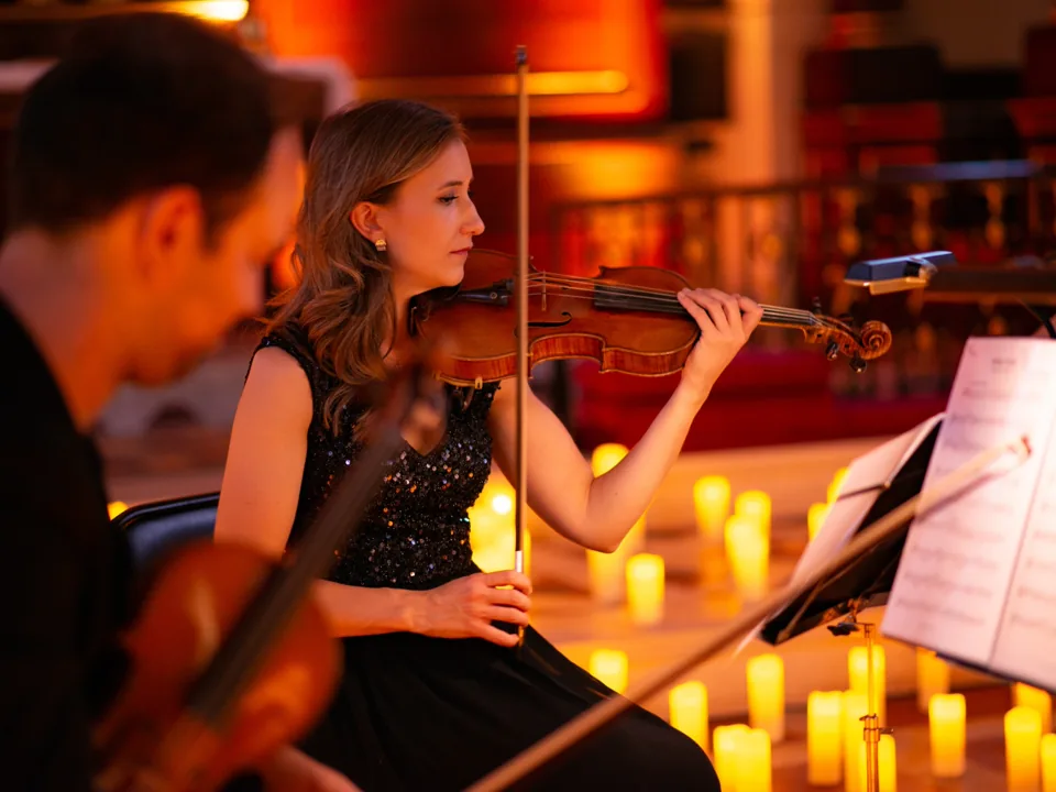 A violinist in black plays among candles at Musicals by Candlelight, The Actors' Church