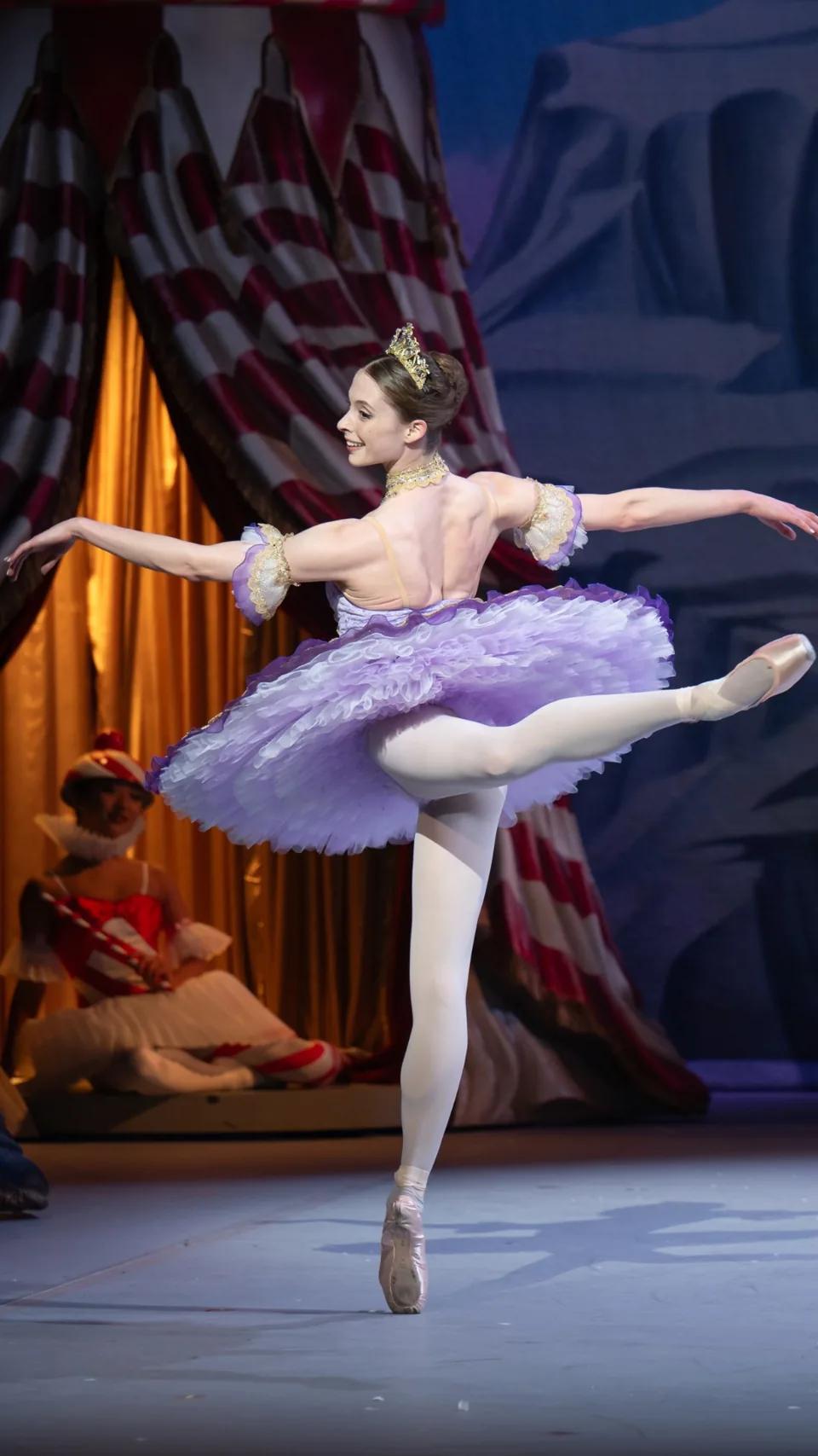 A ballerina in a lilac tutu and tiara holds an arabesque in Nutcracker, London Coliseum