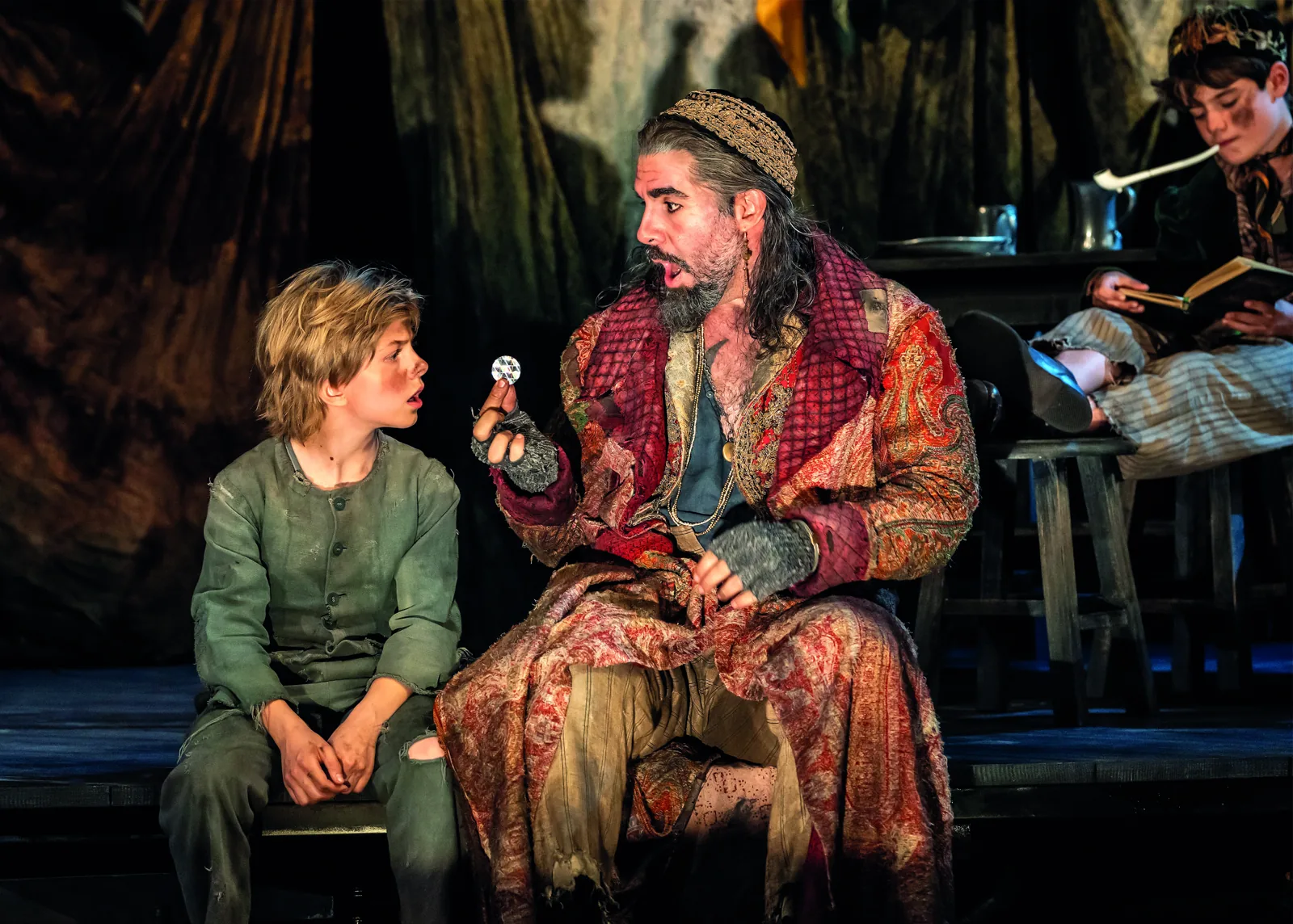 Fagin shows Oliver a glittering trinket in his den, Oliver! at the Gielgud Theatre