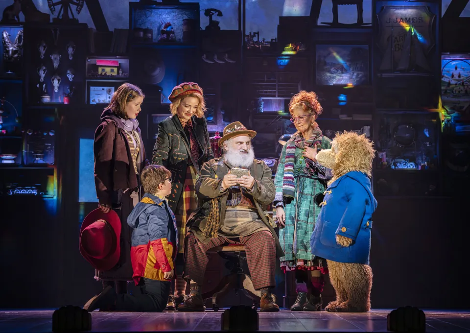 A family and Paddington gather round a seated old man, Paddington The Musical, Savoy Theatre
