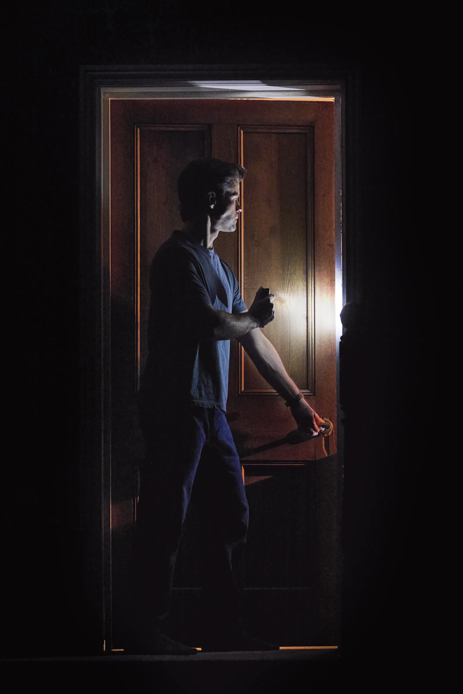 A man stands in a backlit doorway in the dark in Paranormal Activity, Ambassadors Theatre