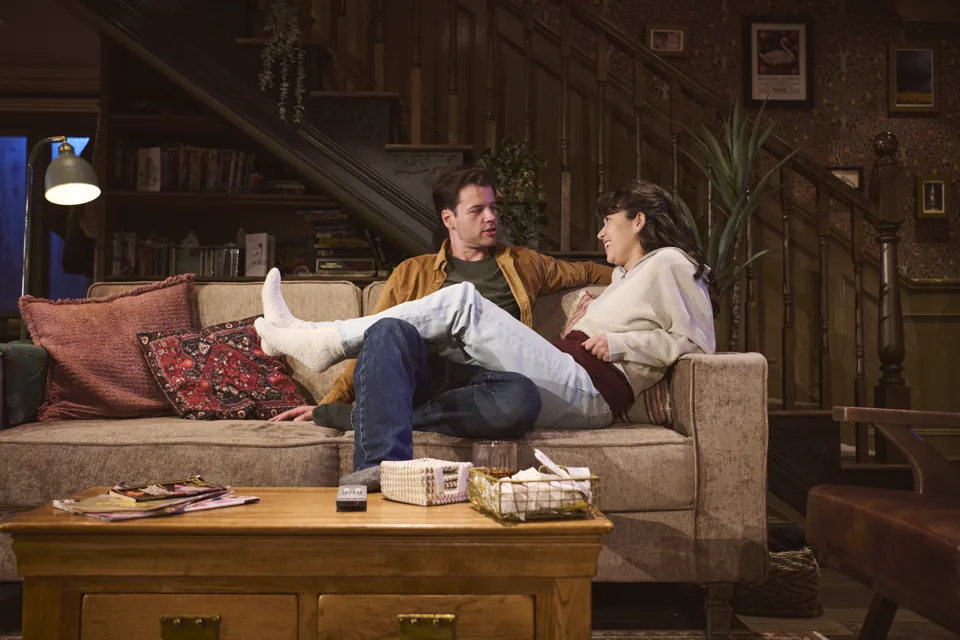 A couple relax on a lamp-lit sofa in Paranormal Activity, Ambassadors Theatre
