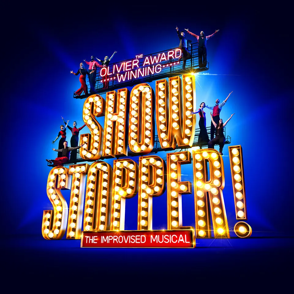 Performers celebrating on bright golden scaffolding in Showstopper! The Improvised Musical at the Cambridge Theatre