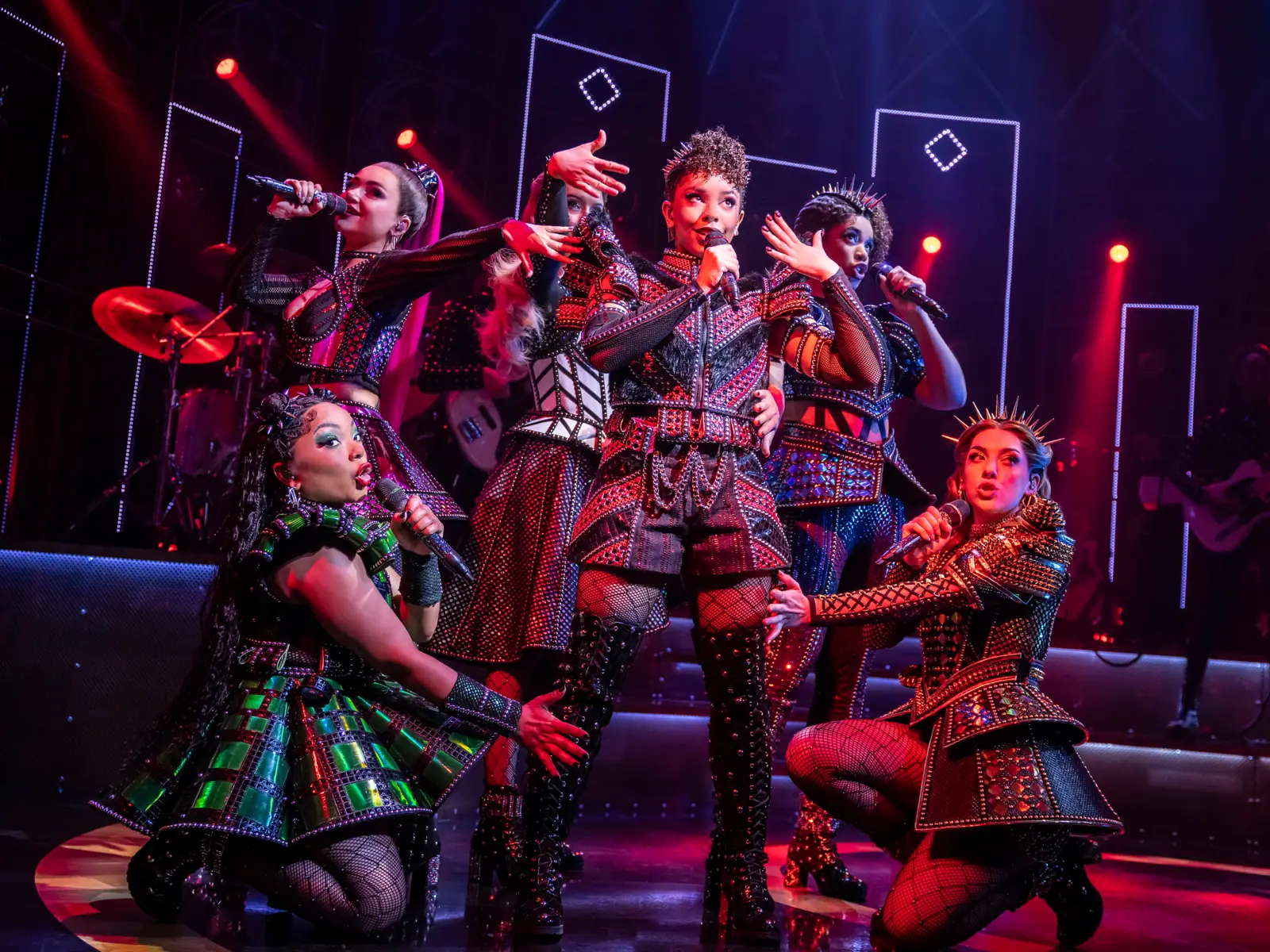 Six queens cluster together singing in red stage light, SIX at the Vaudeville Theatre