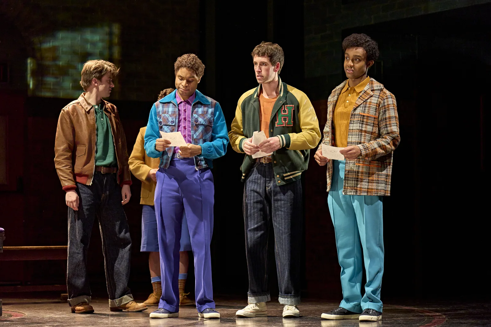 Four young men in bright 1950s jackets read notes in Stranger Things, Phoenix Theatre