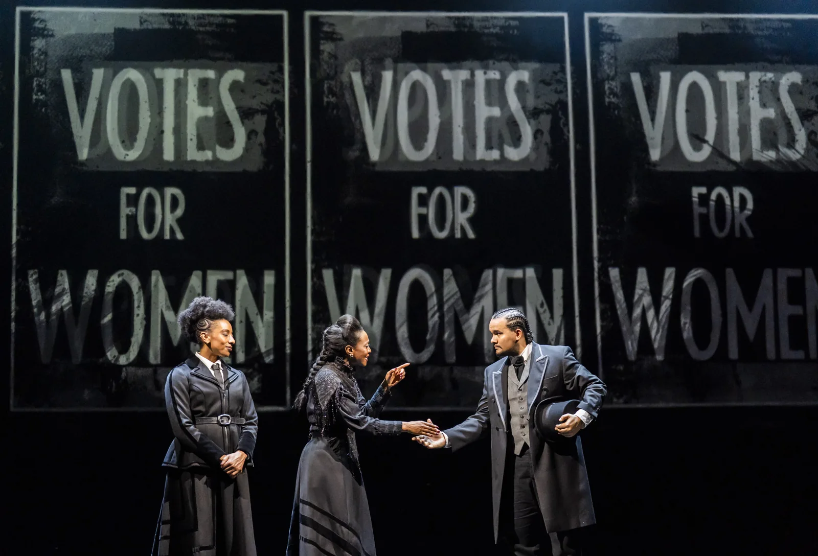 Three performers argue in front of Votes for Women posters in Sylvia, Royal Albert Hall
