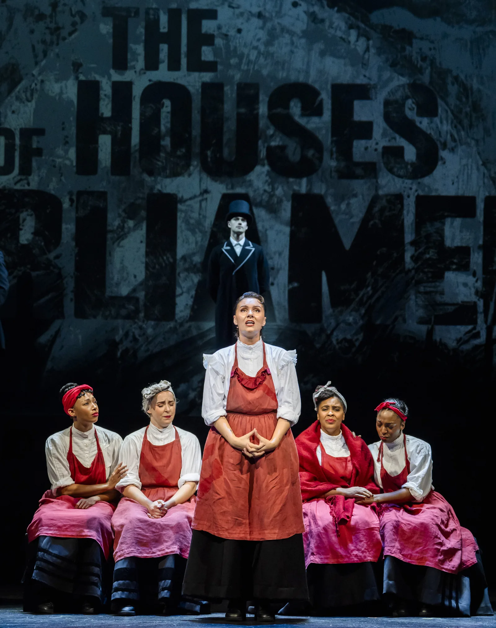 A woman in a red apron sings among seated women in Sylvia, Royal Albert Hall