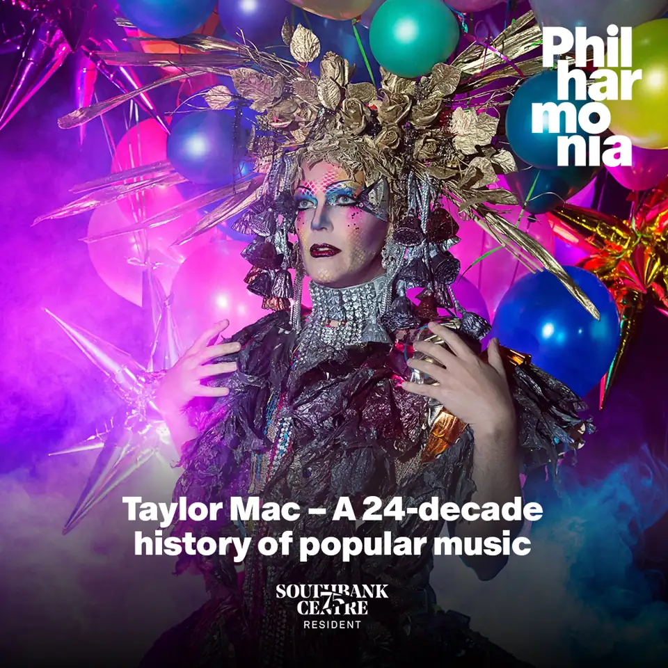 Performer in elaborate gold headdress and embellished costume against neon pink and blue lighting in Taylor Mac – A 24-decade history of popular music at the Royal Festival Hall - Southbank Centre
