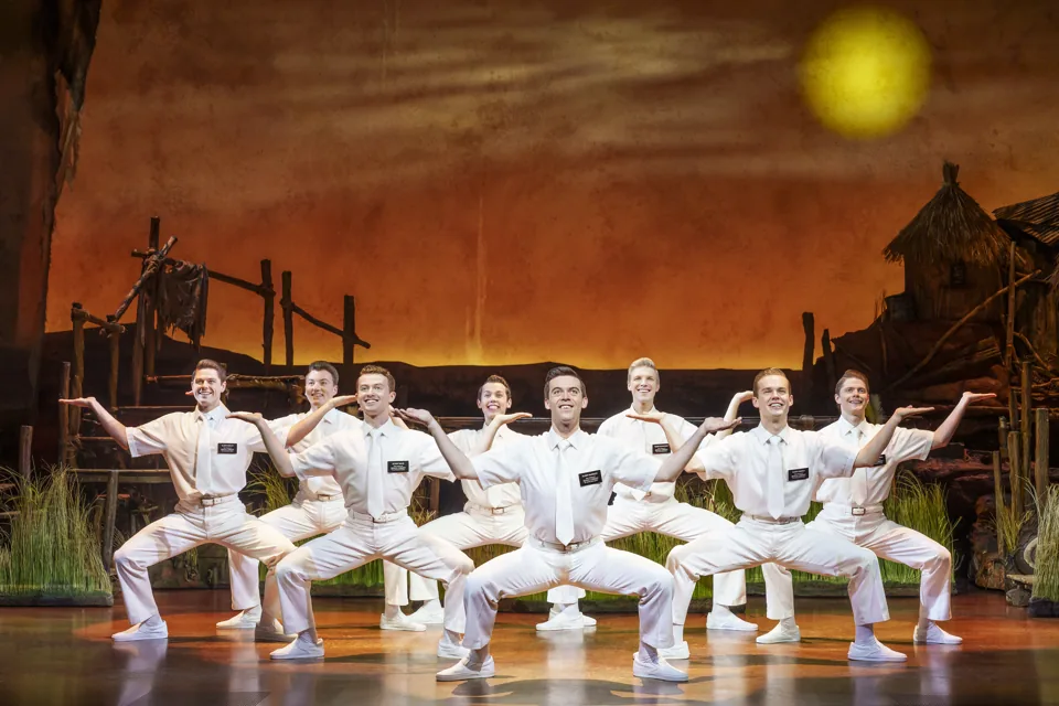 White-suited missionaries crouch in a row, The Book of Mormon, Prince of Wales Theatre