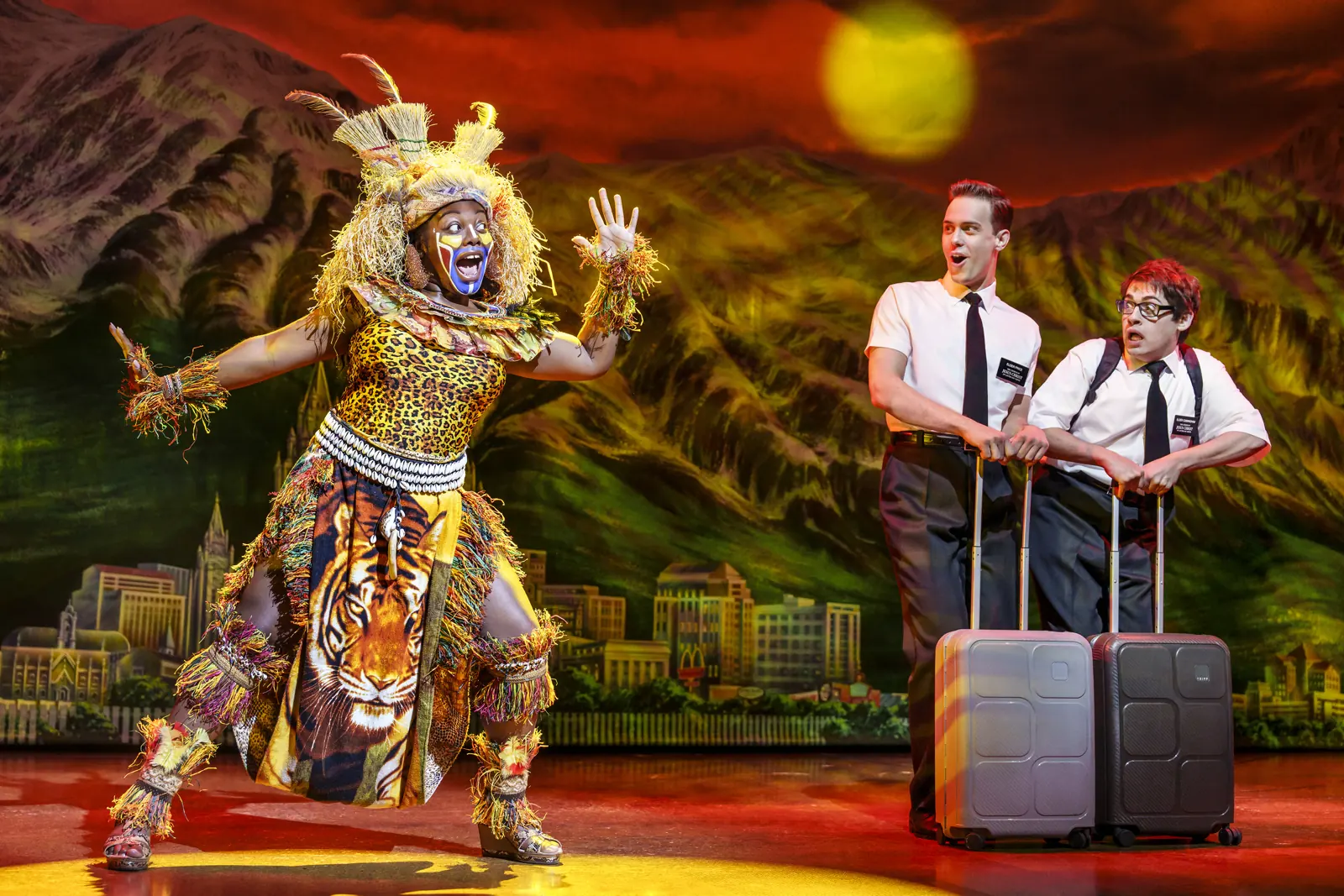 Suitcase-toting missionaries meet a costumed dancer, The Book of Mormon, Prince of Wales Theatre