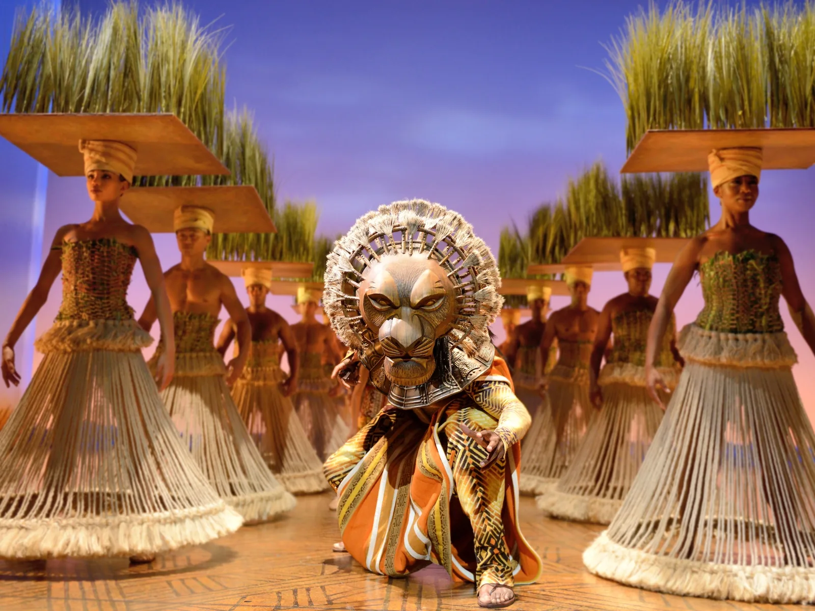 A performer in a lion headdress crouches among grassland dancers, The Lion King, Lyceum Theatre