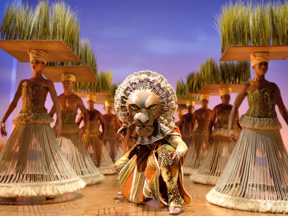 A performer in a lion headdress crouches among grassland dancers, The Lion King, Lyceum Theatre