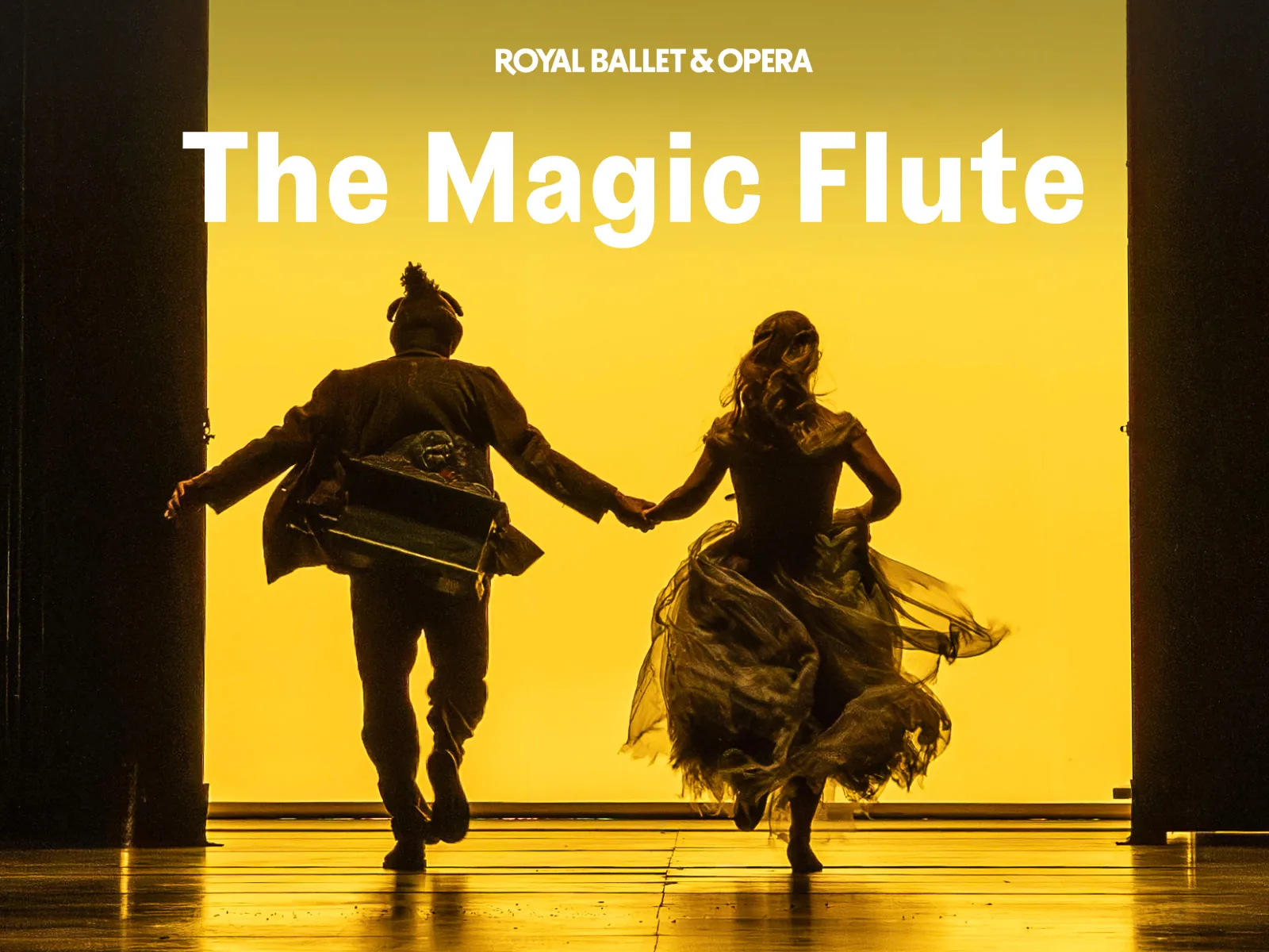Two dancers in silhouette hold hands against a golden backdrop in The Magic Flute - Royal Ballet and Opera at the Royal Opera House
