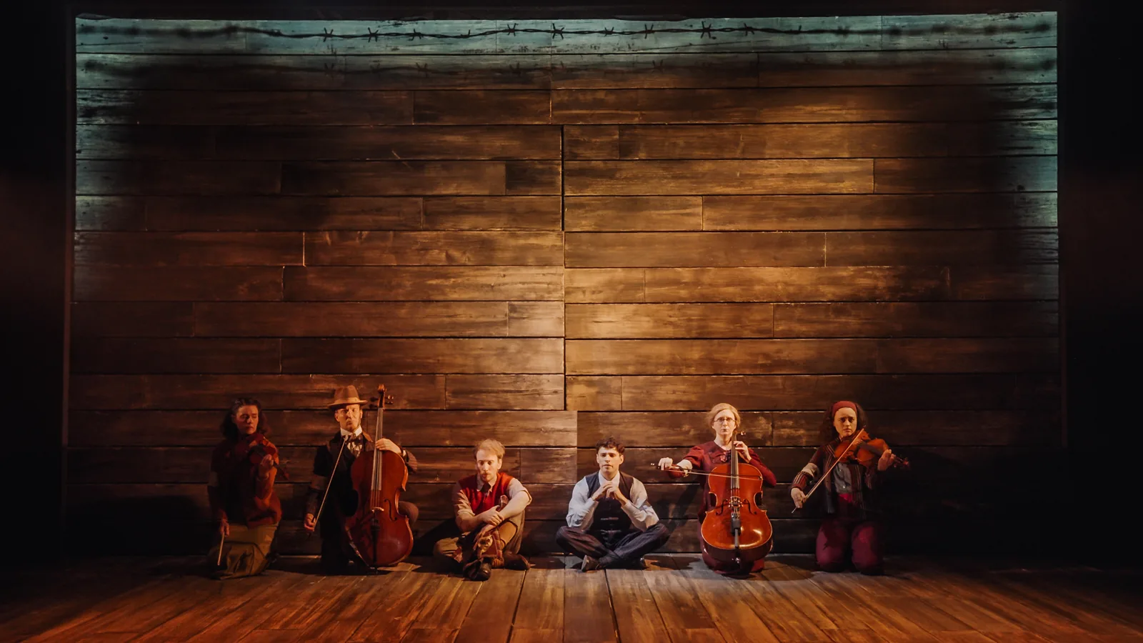 Six players sit against a wooden wall with their instruments in The Pianist, Park Theatre