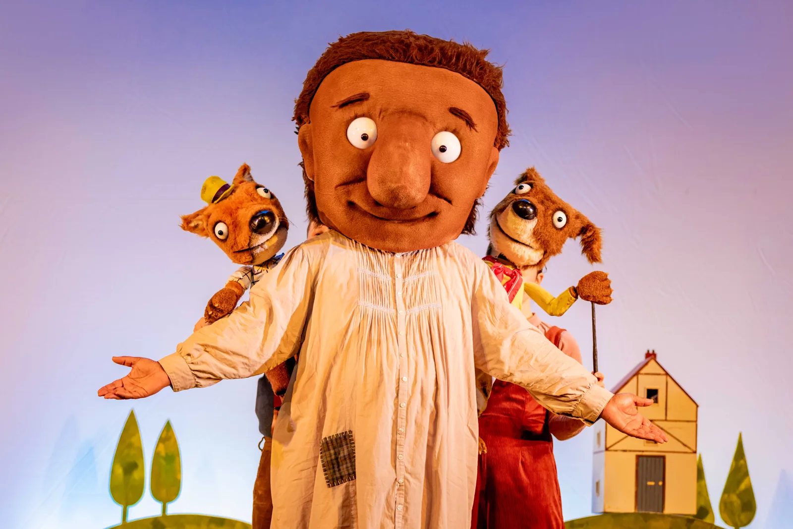 George holds two animal puppets by a yellow house: The Smartest Giant in Town, St. Martin's