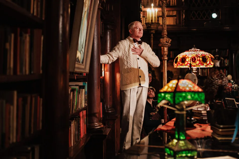 Jesse Tyler Ferguson as Truman Capote, hand on heart, by the bookshelves, Tru, Menier Chocolate Factory