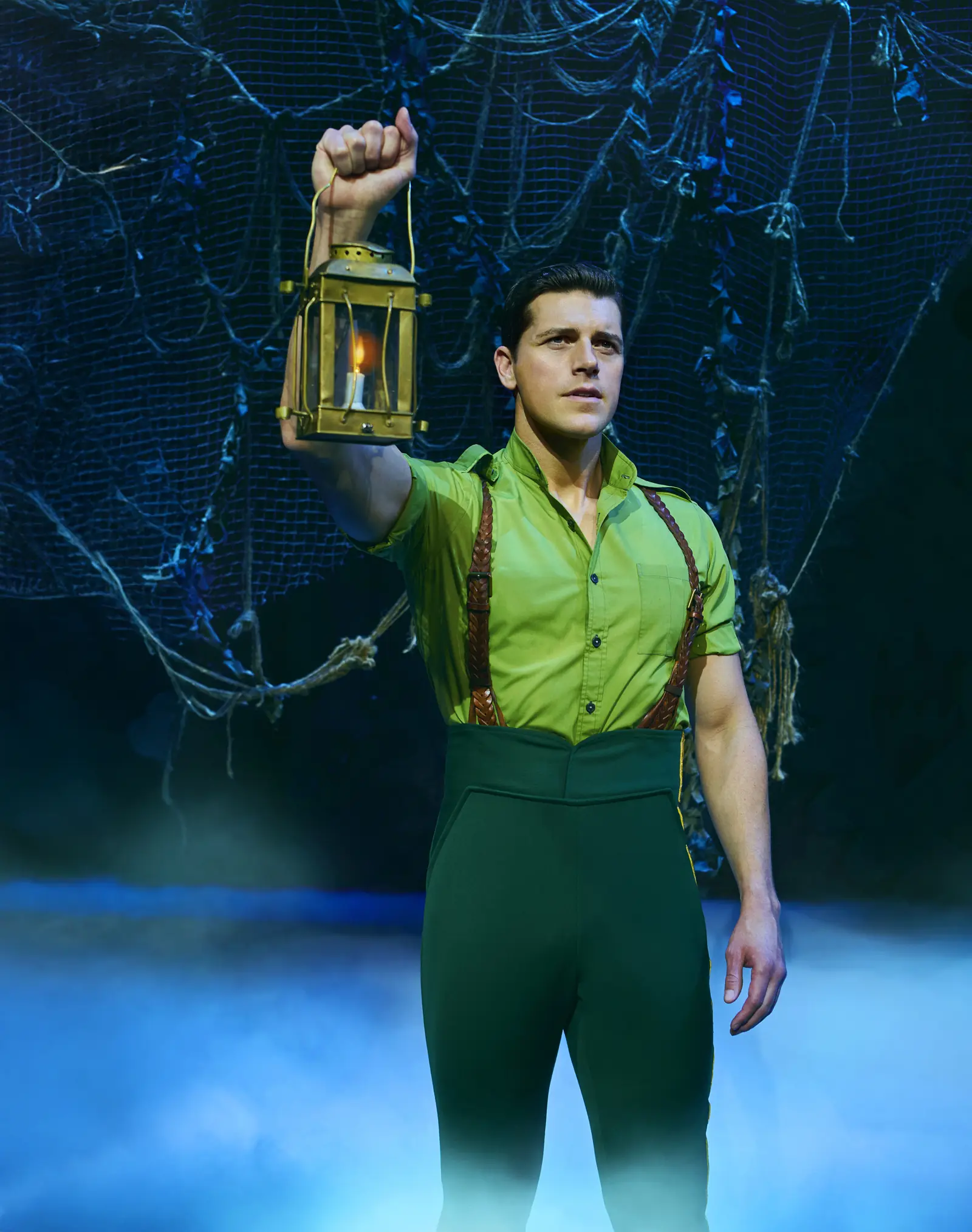 Jordan Litz as Fiyero raises a lantern in the mist, Wicked, Apollo Victoria Theatre