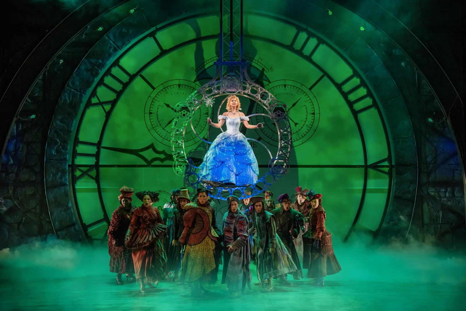 Zizi Strallen's Glinda floats above the company by a green clock, Wicked, Apollo Victoria