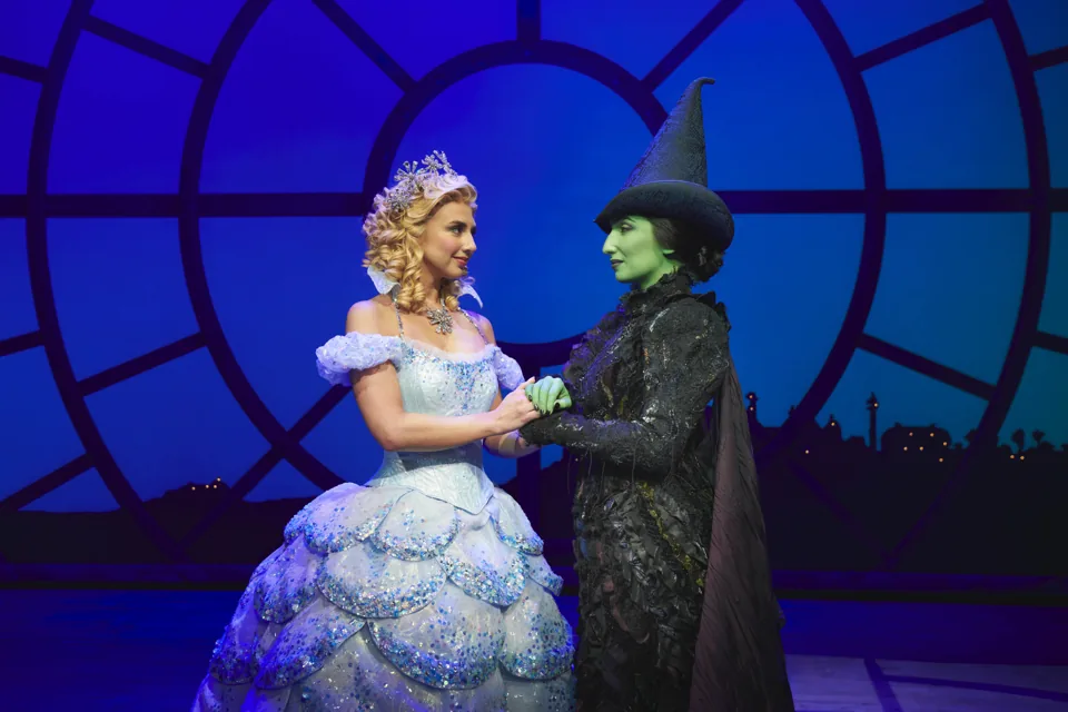 Zizi Strallen as Glinda and Emma Kingston as Elphaba hold hands, Wicked, Apollo Victoria